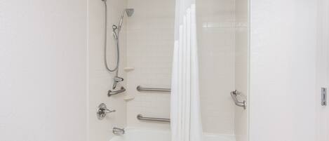 A white bathroom with a bathtub, shower, and handrails.
