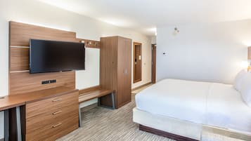 Quarto de hotel com cama, escrivaninha com gavetas, televisão fixada na parede e guarda-roupa.