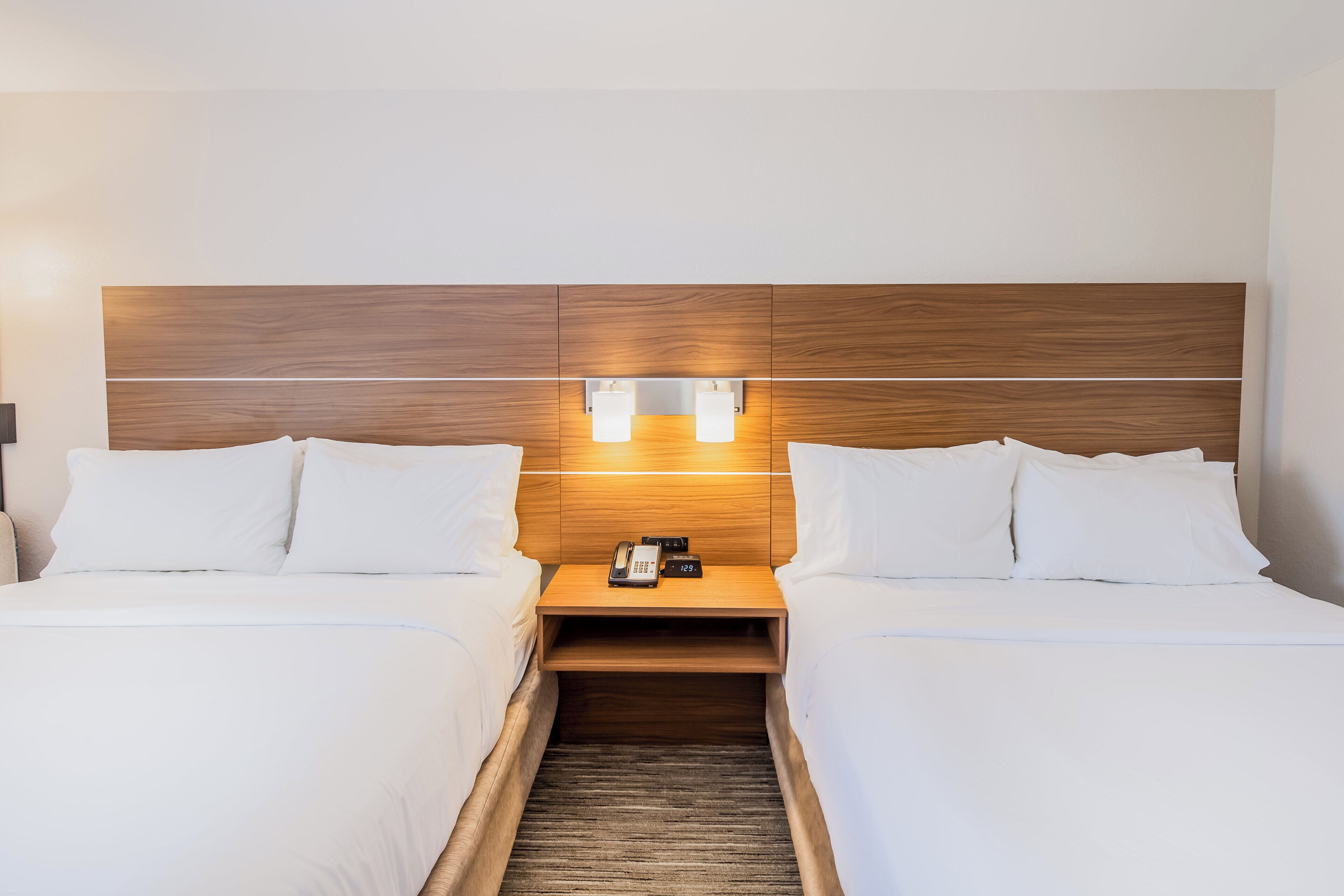 Habitación de hotel con dos camas, cabecero de madera, lámparas de noche y un teléfono en la mesita.