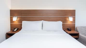 A hotel room with a wooden headboard, two bedside tables, a bed with white linens, and a small nightstand with a telephone and a clock.
