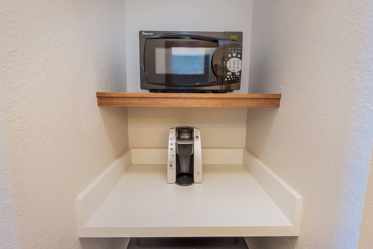 Un microondas sobre una estantería, encima de una cafetera.
