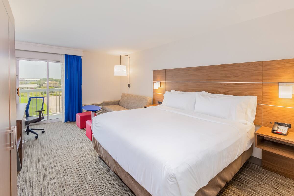 Habitación de hotel con una cama grande, un escritorio, una silla y vistas al exterior.