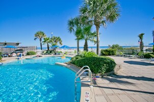 A pool area with palm trees, lounge chairs, and a clear blue sky.