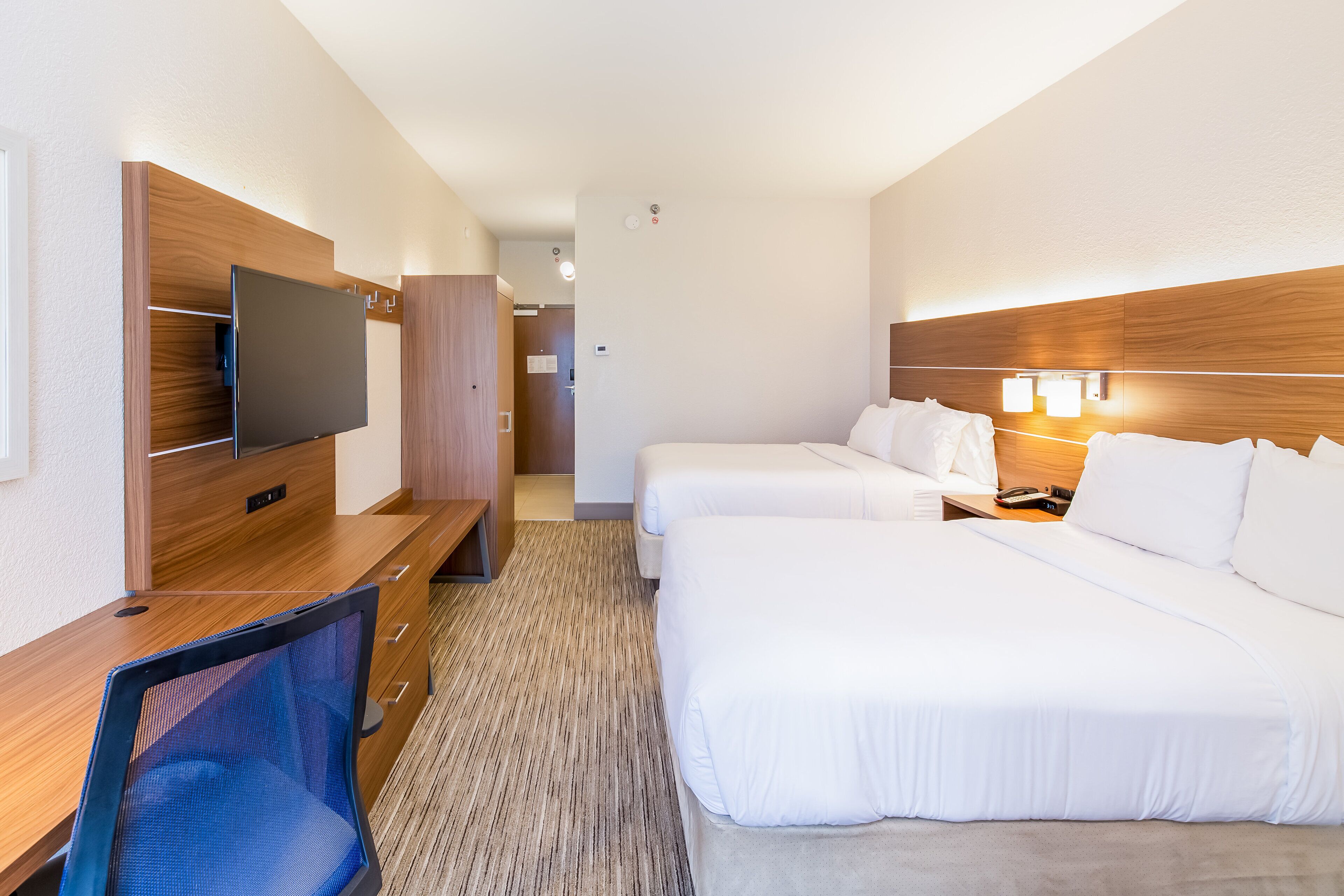 Habitación de hotel con dos camas, un escritorio con silla, televisor y cabecera de madera.