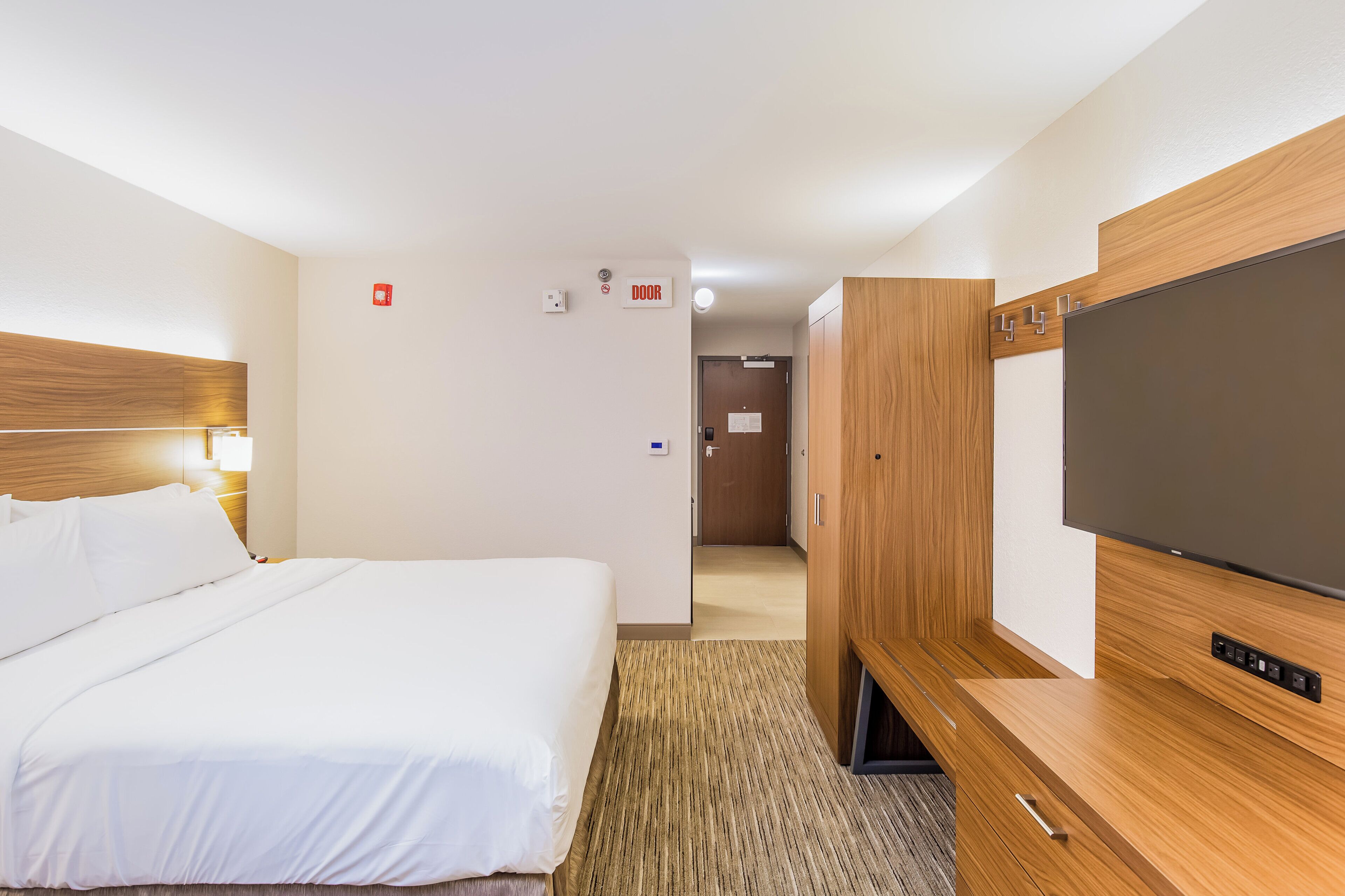 Een hotelkamer met een bed, een televisie, een kledingkast en een deur met een bordje.