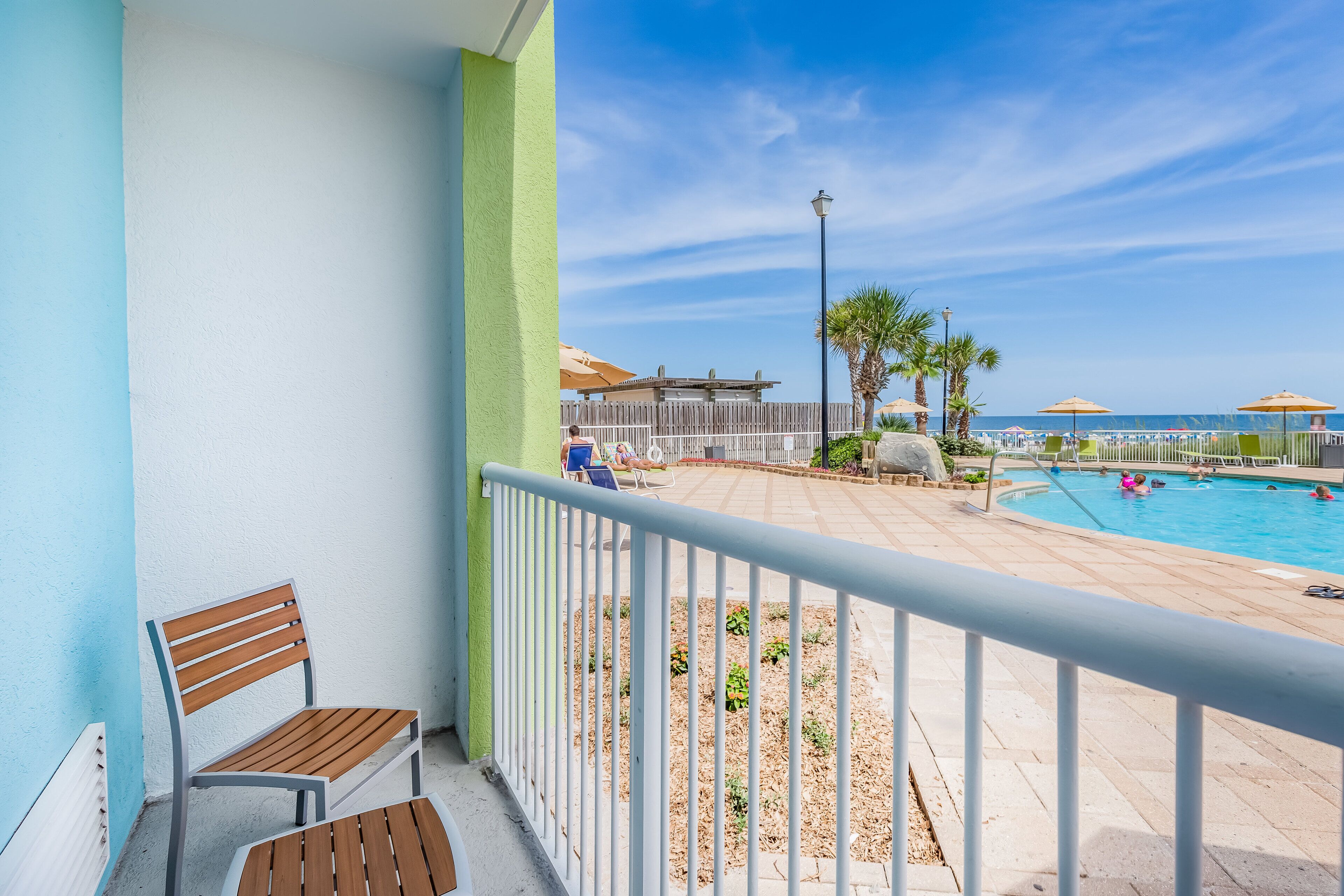 A balcony with a view of a swimming pool and beach umbrellas.