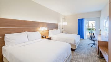 A hotel room with two beds, a desk, a chair, a lamp, and a view of an outdoor area.