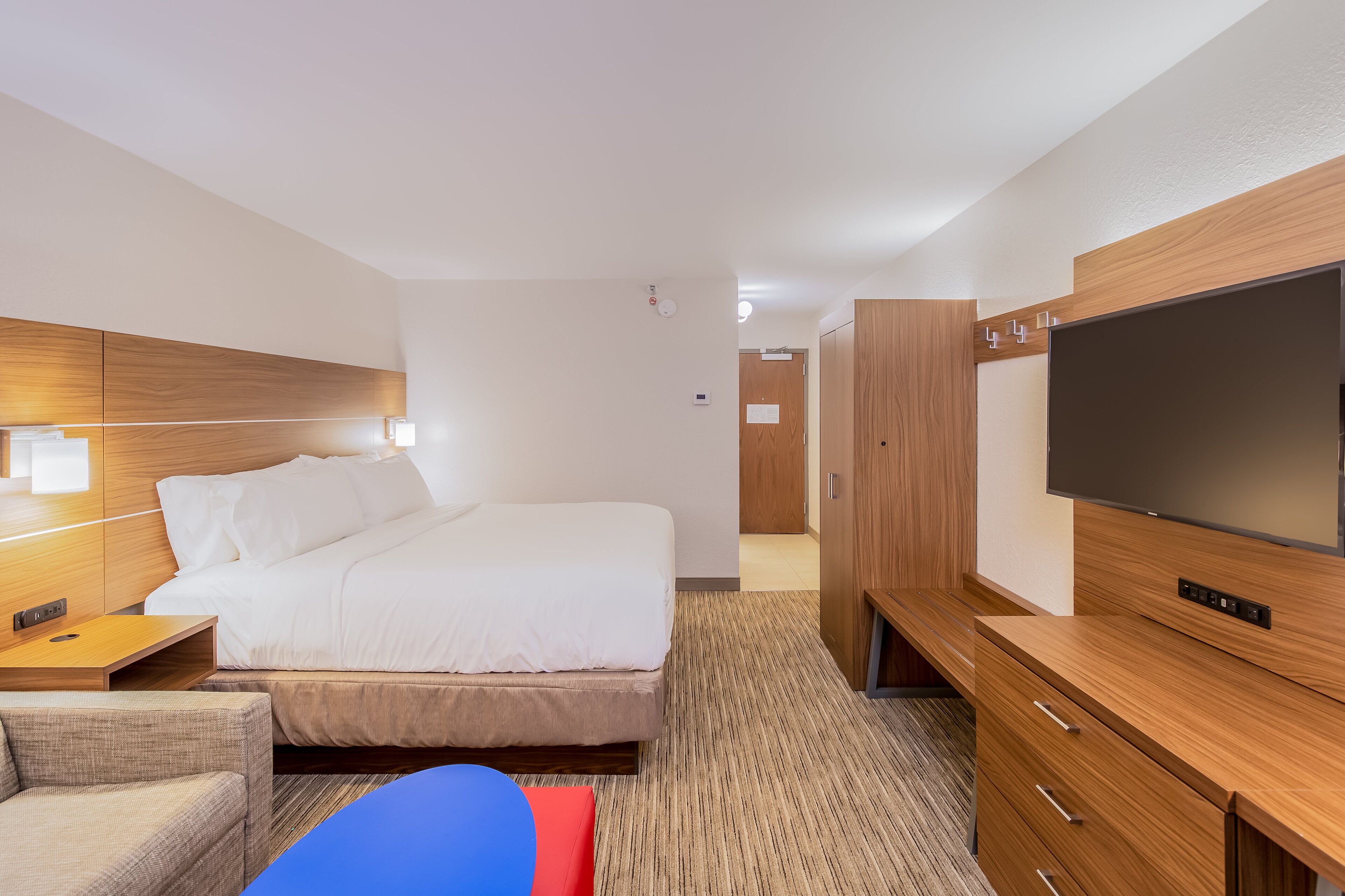 A hotel room with a bed, bedside table, TV, wardrobe, and a small seating area.