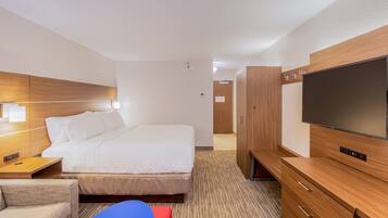 A hotel room with a bed, bedside table, TV, wardrobe, and a small seating area.