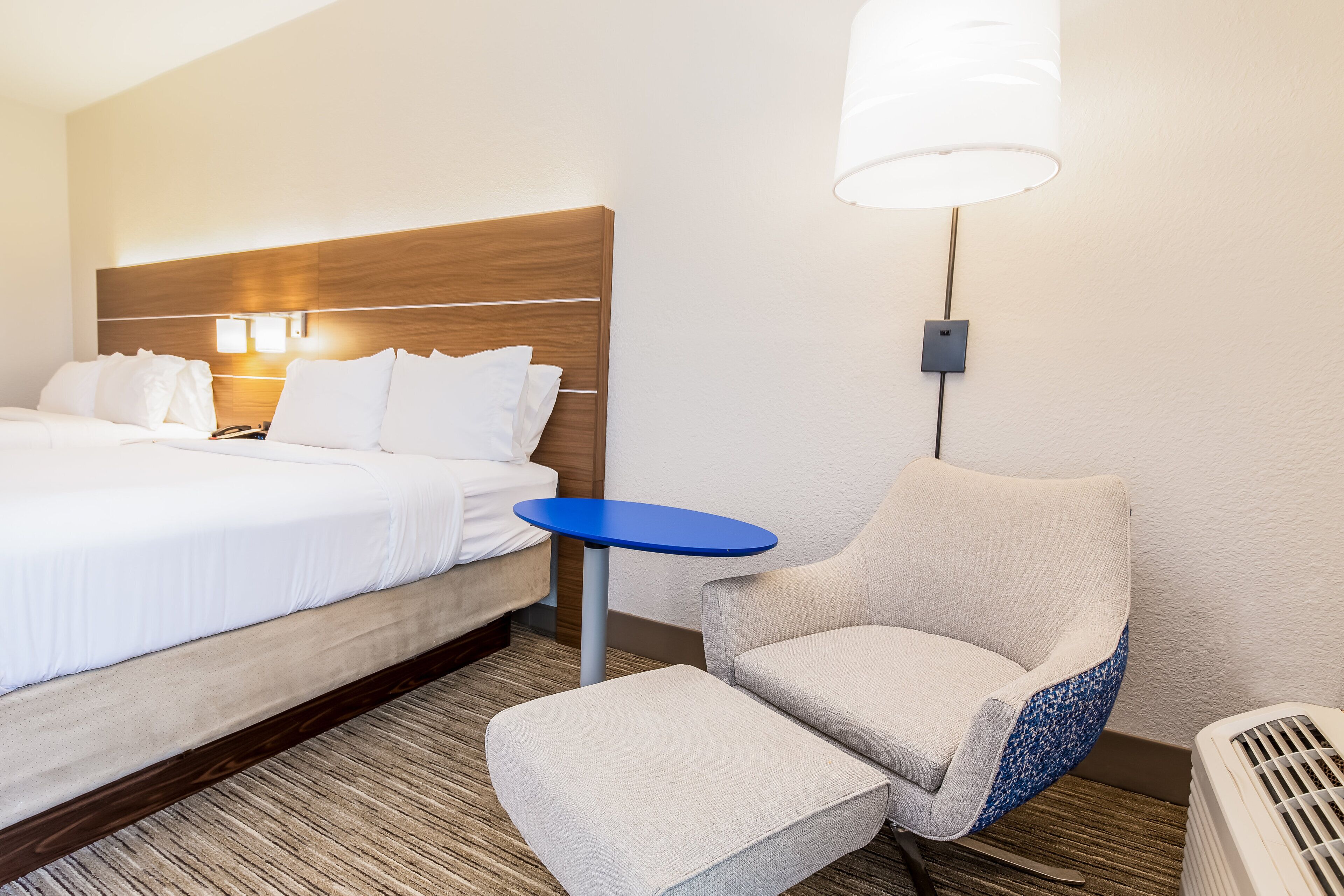 Una habitación de hotel con una cama, una mesita pequeña azul, una silla y un calentador.