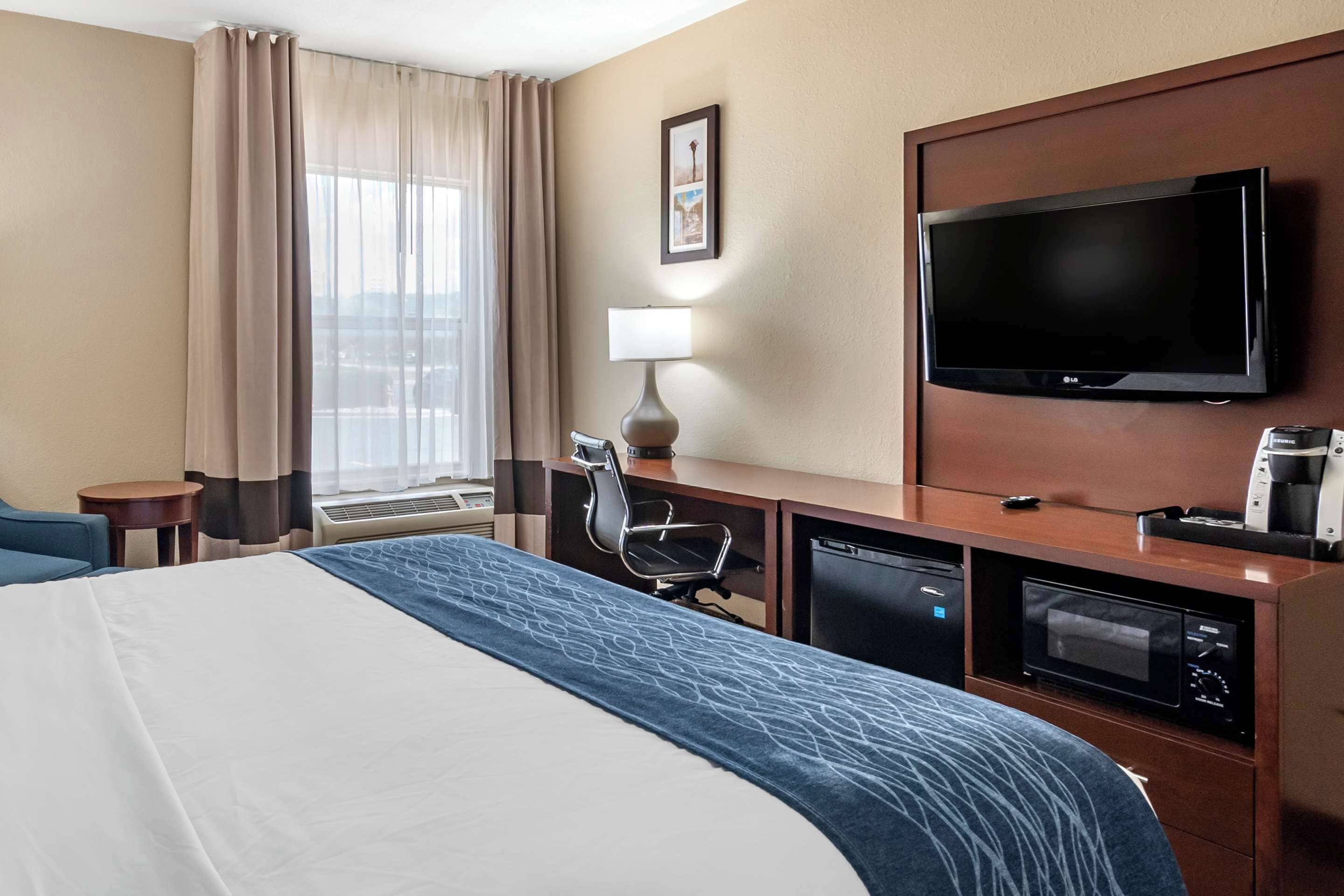 Habitación de hotel con cama, escritorio con lámpara, televisión, microondas y cafetera.