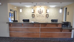 Una recepción de hotel con pared de piedra de fondo, dos monitores de ordenador y un tapete de bienvenida.