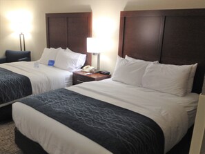 A hotel room with two beds, a desk, and a nightstand with a lamp and phone.