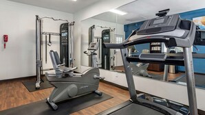 Un gimnasio con equipamiento de ejercicio, una cinta de correr y un espejo.