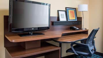 Habitación de hotel con un escritorio de madera, un televisor de pantalla plana, una silla de oficina negra, una lámpara y un cuadro en la pared.