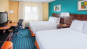 Een hotelkamer met twee bedden, een bureau met een televisie, een stoel en een kamerbreed tapijt met een patroon.