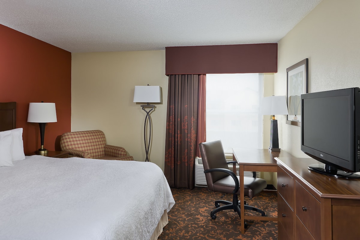 A hotel room with a bed, a desk with a chair, a television, and a floor lamp.