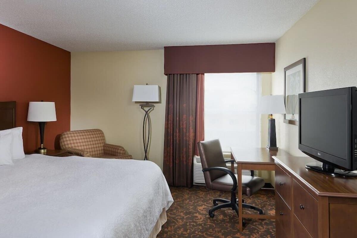 A hotel room with a bed, a desk, a chair, a television, and a lamp.