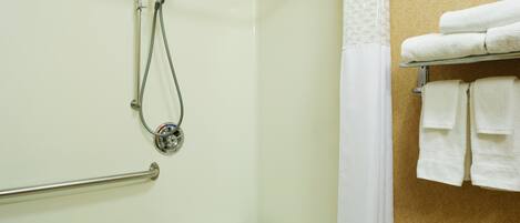 A bathroom with a shower, grab bars, a towel rack, and a patterned wall.