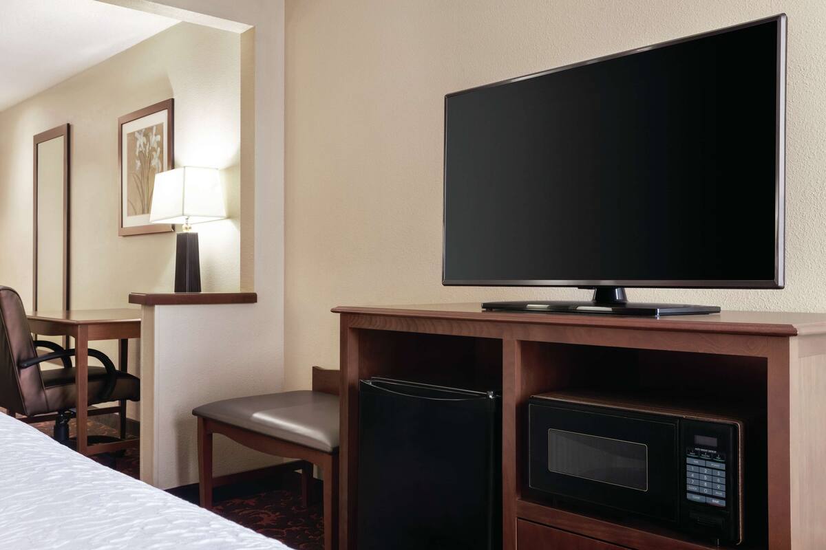 A hotel room with a bed, a desk with a television, a microwave, and a chair.