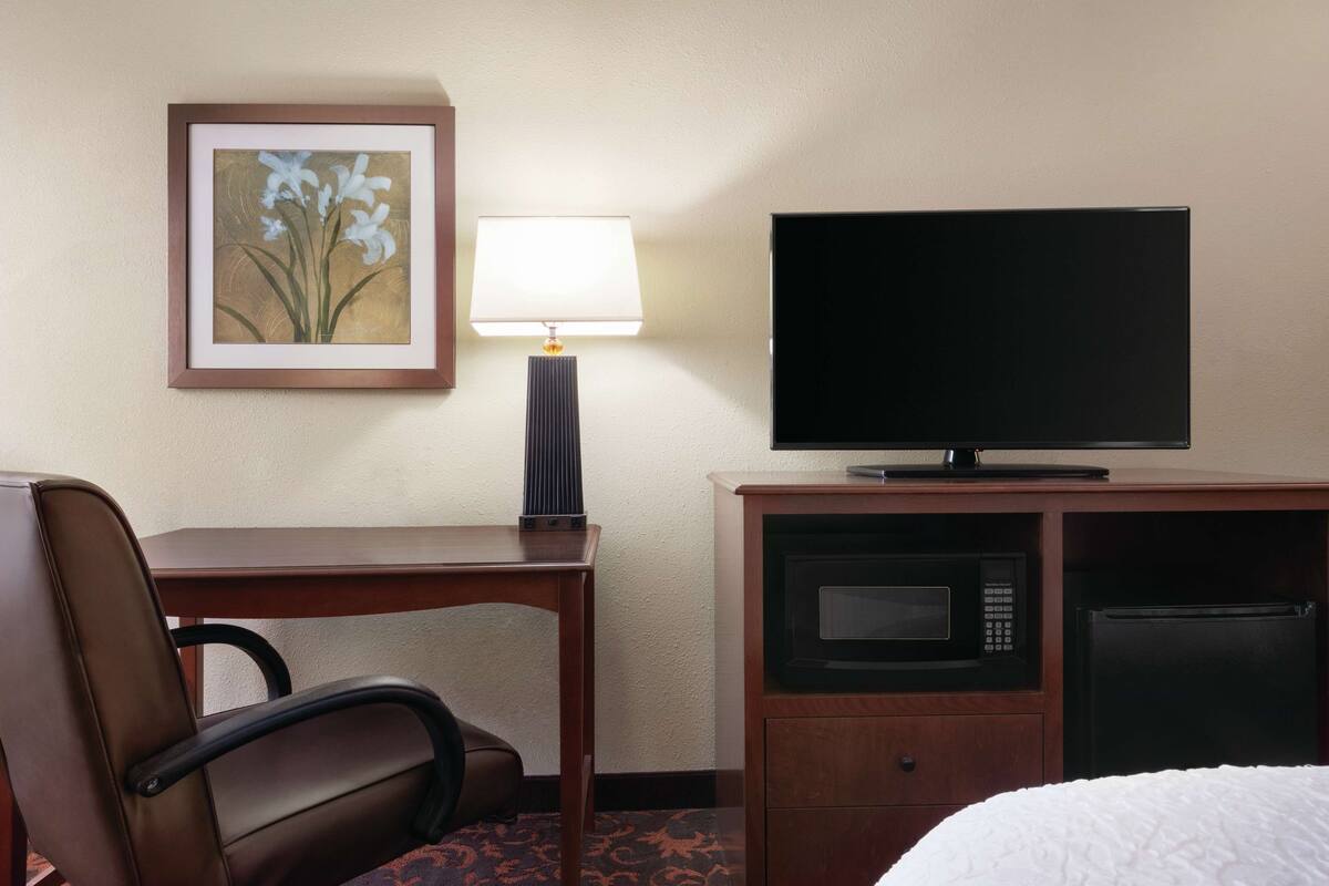 A hotel room with a desk, chair, television, microwave, and refrigerator.