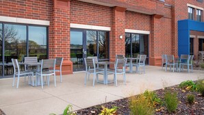 A brick building with outdoor seating and large windows. - Hampton Inn West Des Moines Lake Drive (West Des Moines)