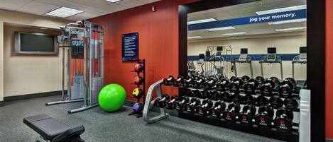 A gym with exercise equipment, a bench, a wall-mounted TV, and a motivational quote.