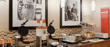 A breakfast buffet with waffle irons, coffee makers, and a variety of food items.