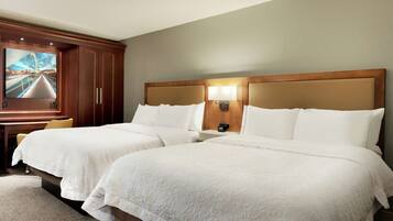 A hotel room with two beds, a TV mounted on the wall, and a desk with a chair.