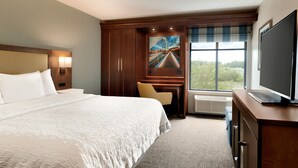 A hotel room with a large bed, a desk, a television, and a window with a view of greenery. - Hampton Inn West Des Moines Lake Drive (West Des Moines)