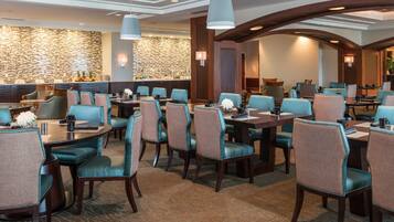 A hotel dining area with multiple tables and chairs, a stone wall, and modern lighting fixtures.
