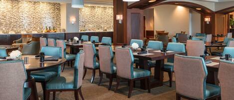 Un comedor de hotel con varias mesas y sillas, una pared de piedra y modernas lámparas.