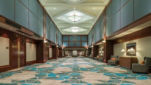 A hotel lobby with a patterned carpet, wooden paneling, and a central chandelier.