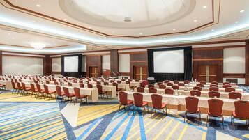 A large conference room with rows of tables and chairs, a stage, and a large screen.