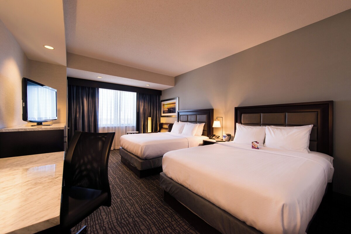 Een hotelkamer met twee bedden, een bureau, een stoel, een televisie en een raam met gordijnen.