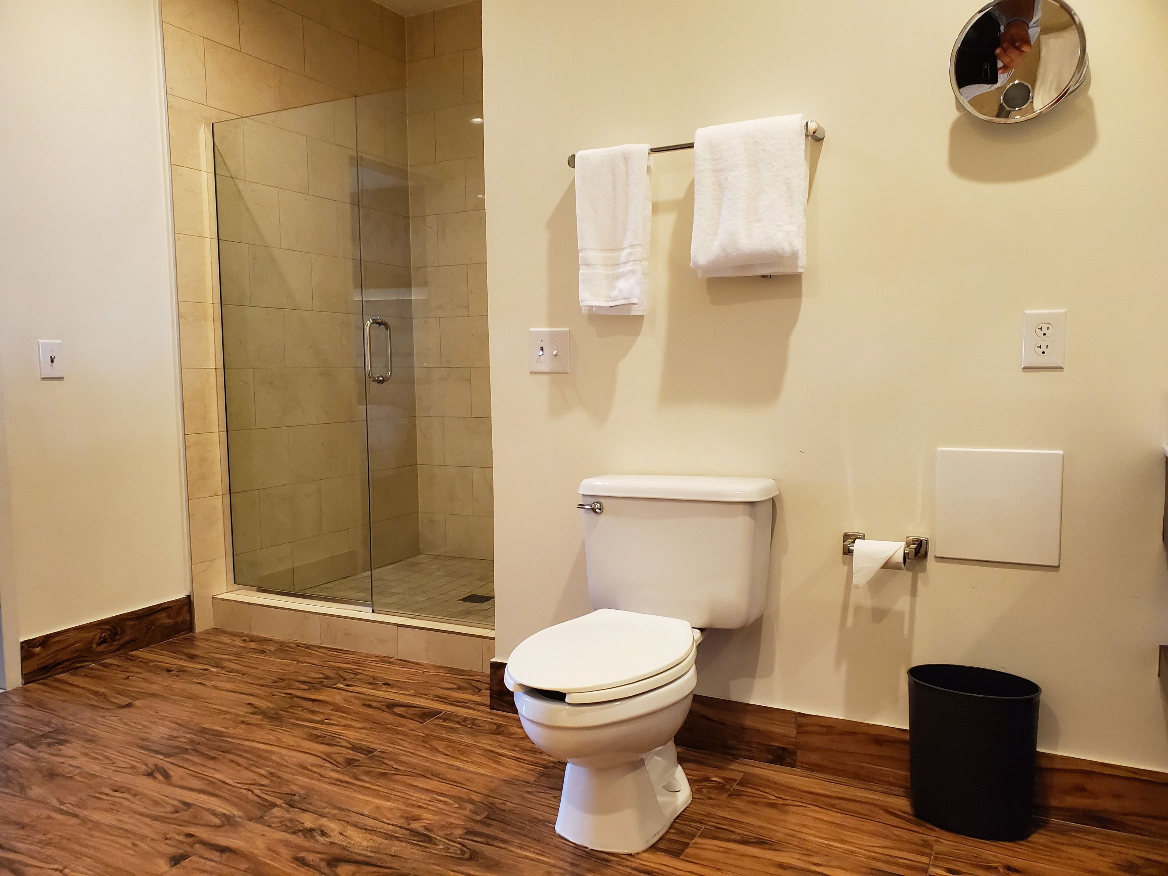 A bathroom with a glass shower enclosure, a toilet, and a black trash can.