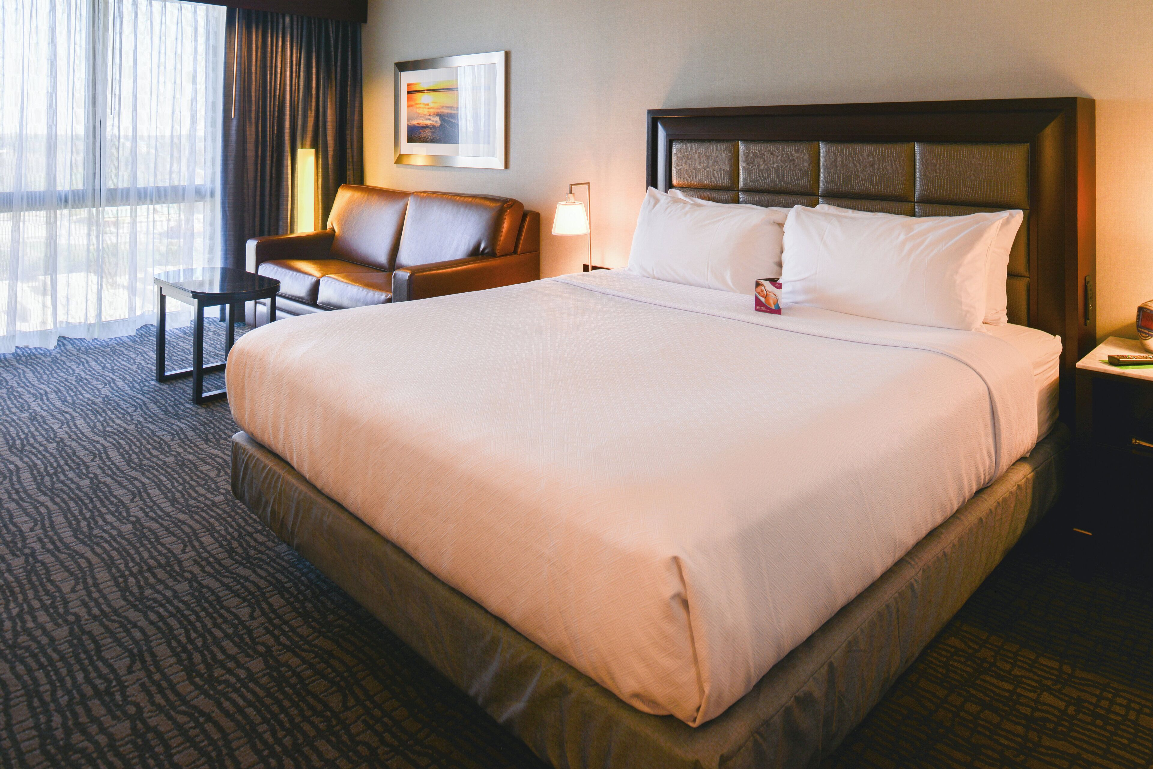 A hotel room with a large bed, a sofa, a small table, and a lamp.