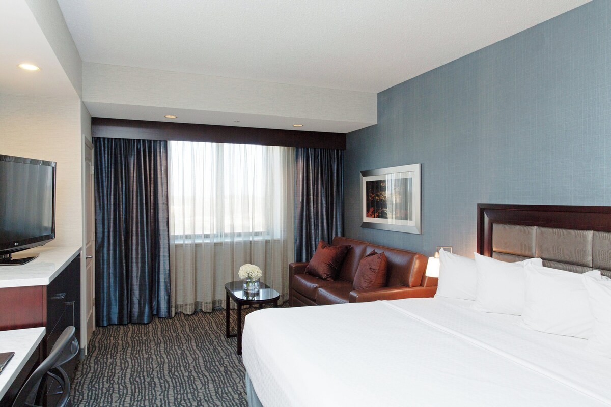 Een hotelkamer met een bed, televisie, bureau, bank en raam met gordijnen.