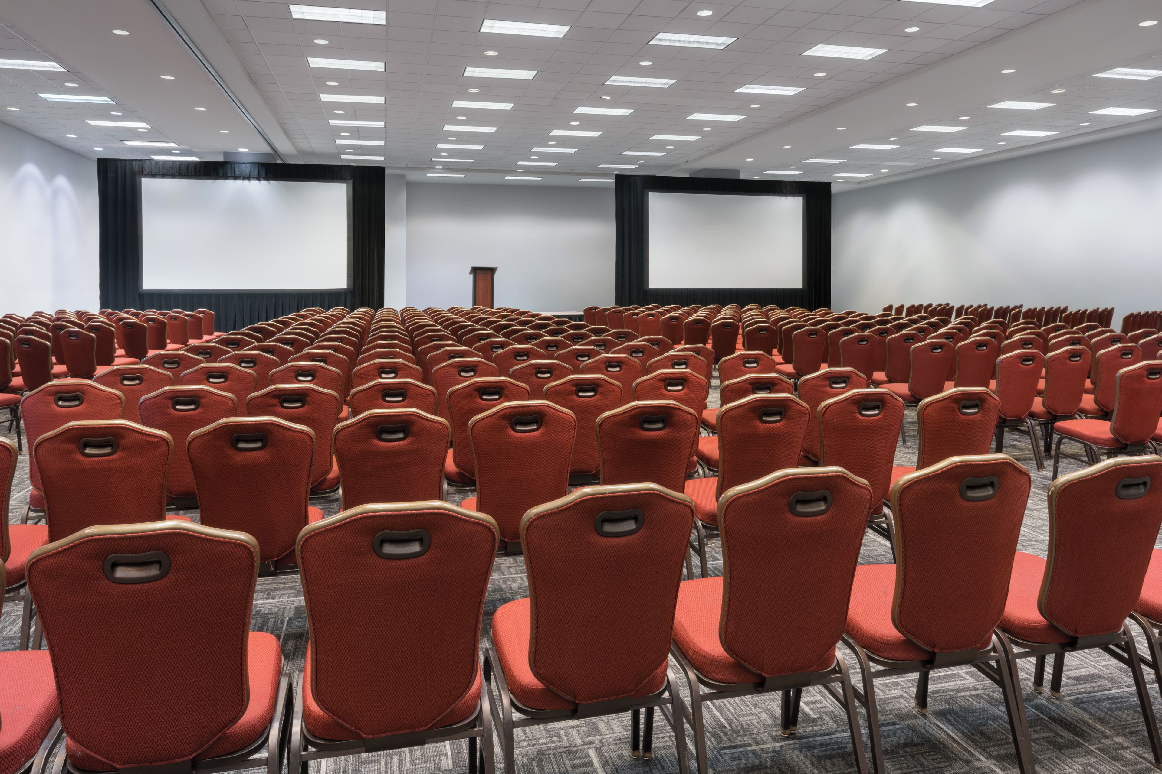 A conference room with rows of red chairs, a large screen, and a podium.