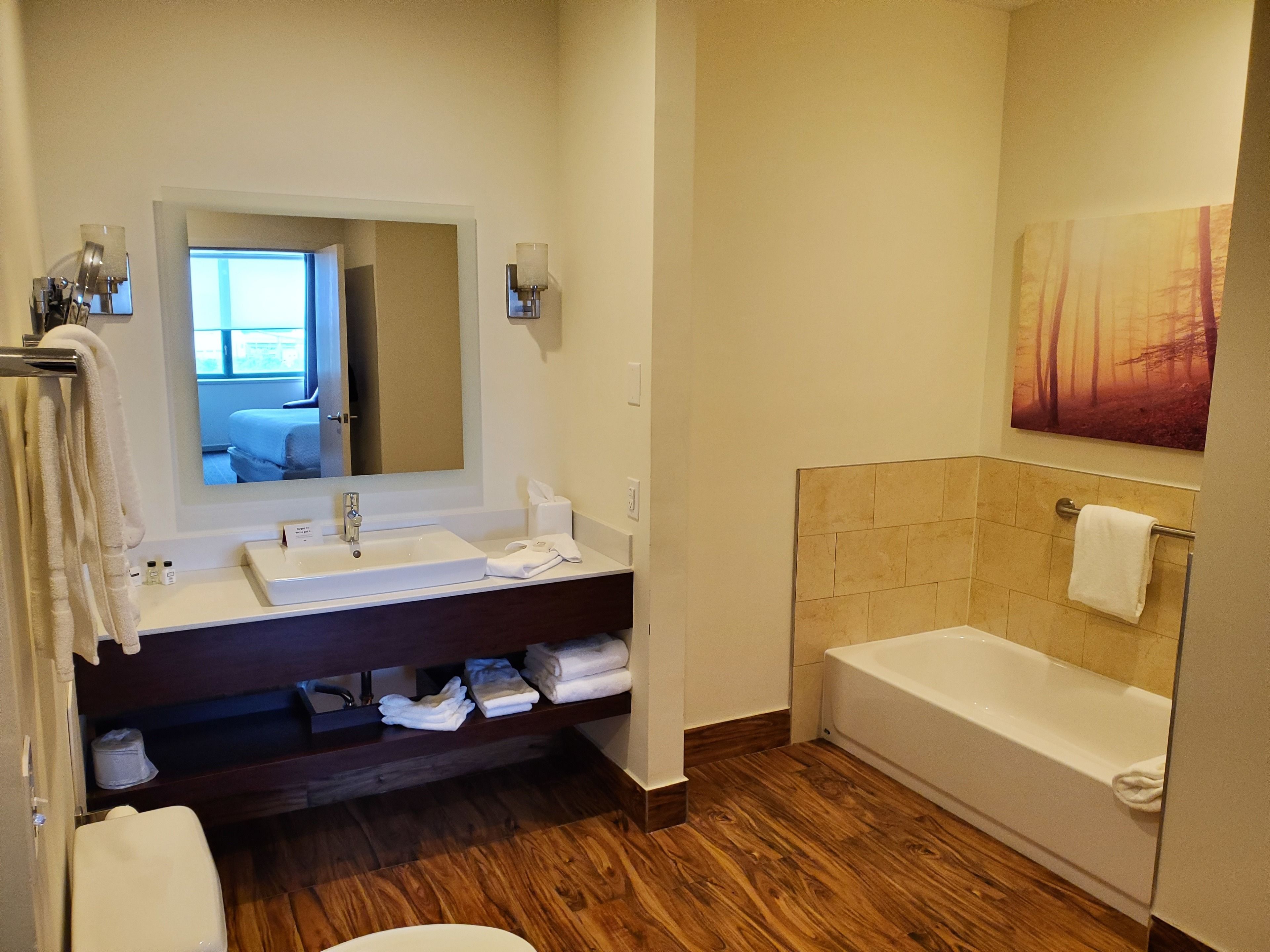 A modern bathroom with a wooden floor, a white sink, a mirror, and a bathtub.