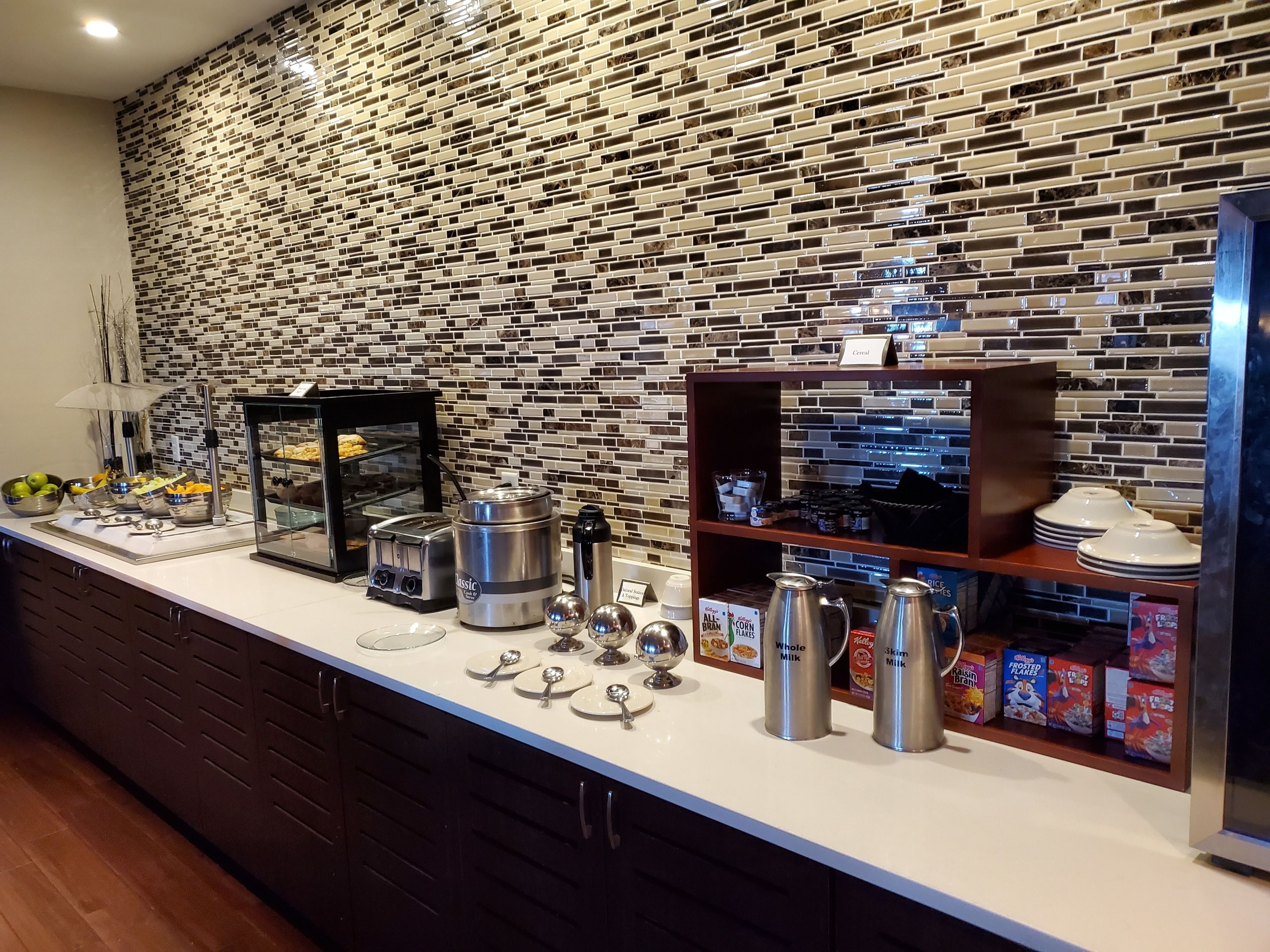 A breakfast buffet area with a variety of food options, including cereal, milk, and bread.