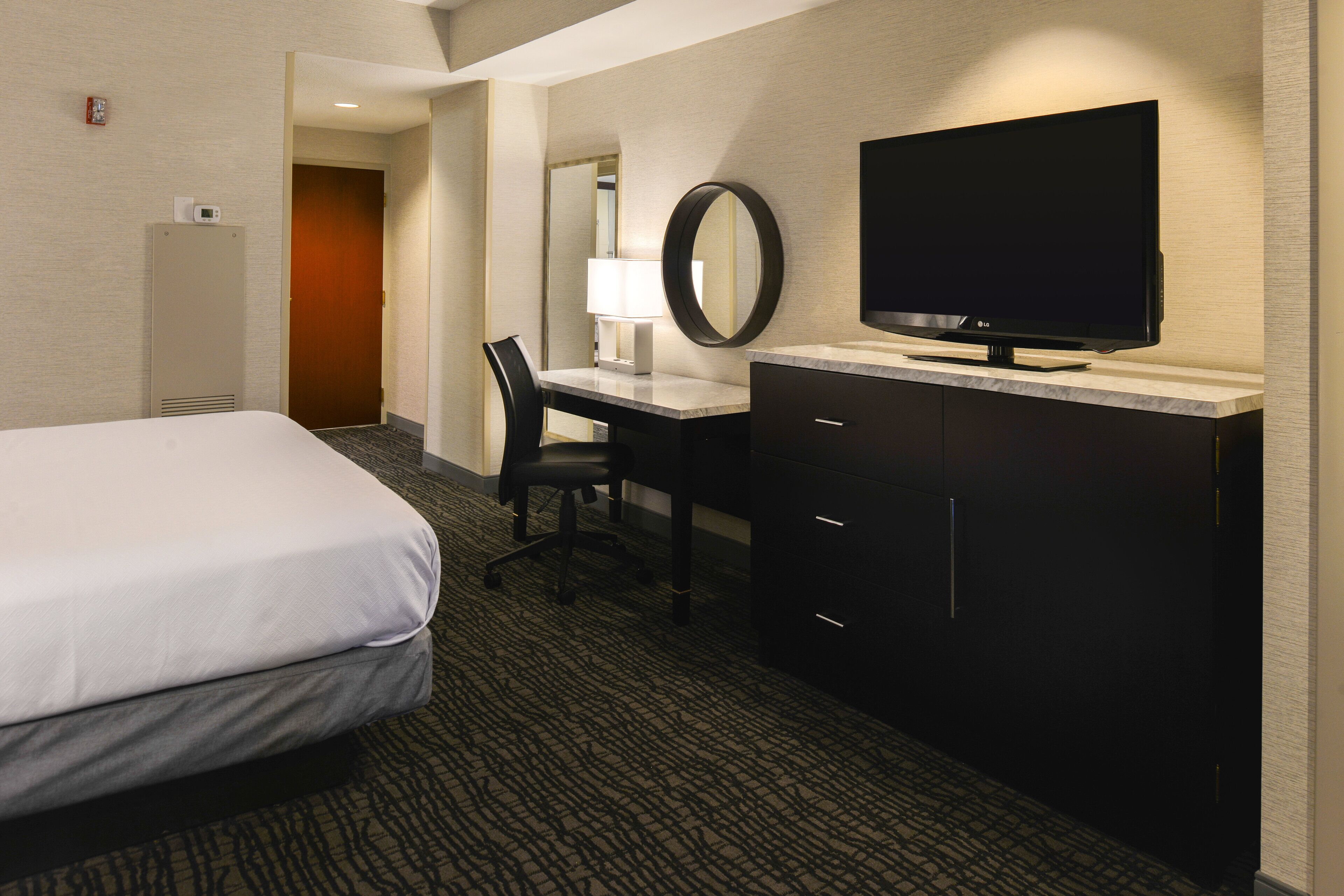 A hotel room with a bed, a desk with a chair, a television, and a mirror.