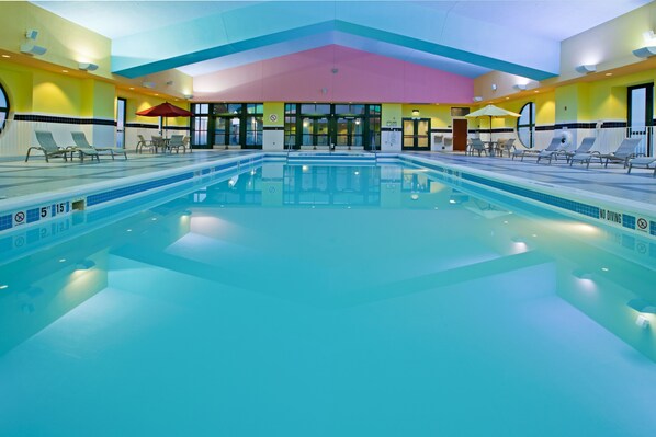 An indoor swimming pool with clear lane markings, multiple lounge chairs, and a colorful ceiling.