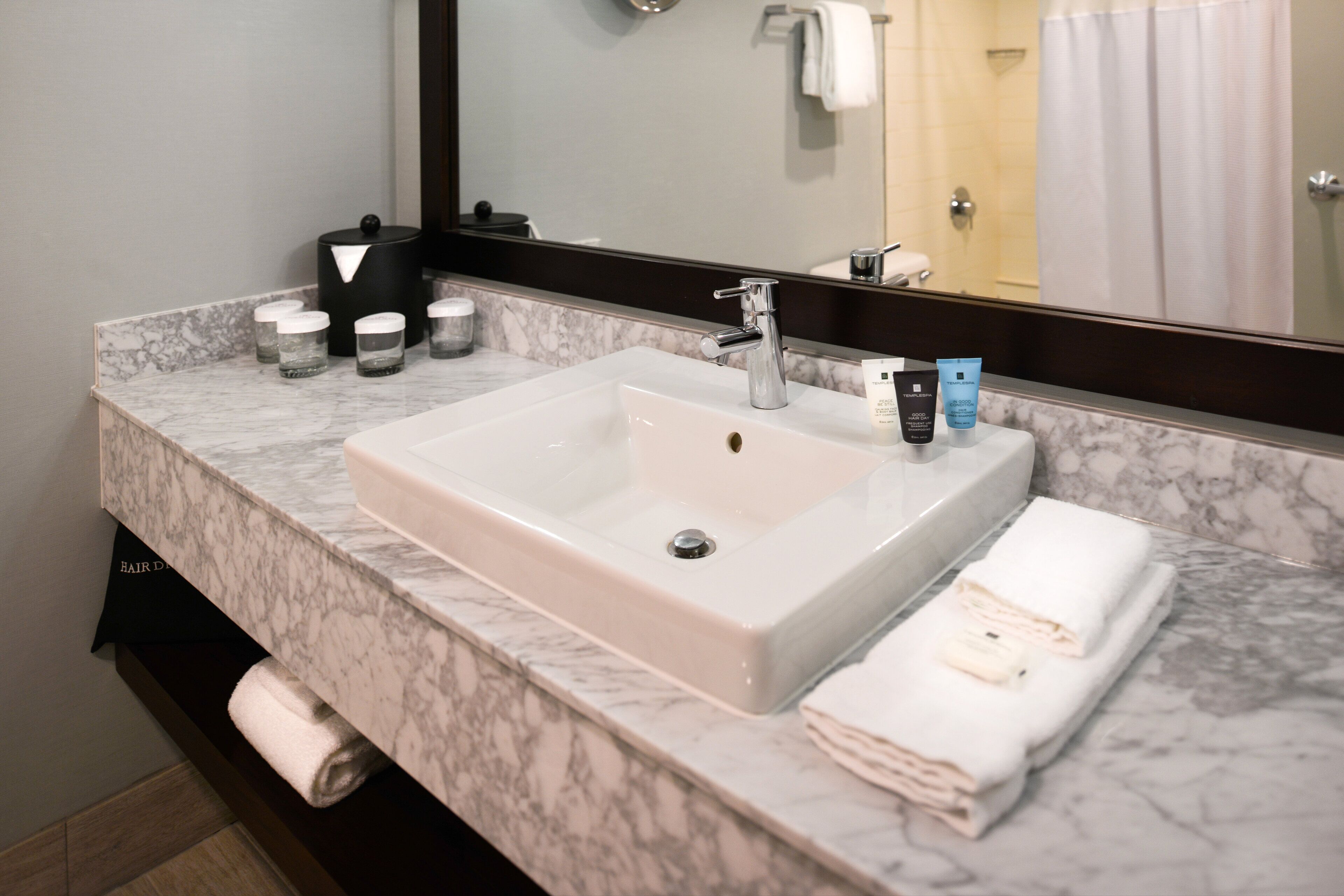 A bathroom with a marble countertop, a white sink, a mirror, and a towel rack.
