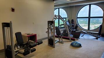 Een sportschool met trainingsapparatuur, grote ramen en stadszicht.