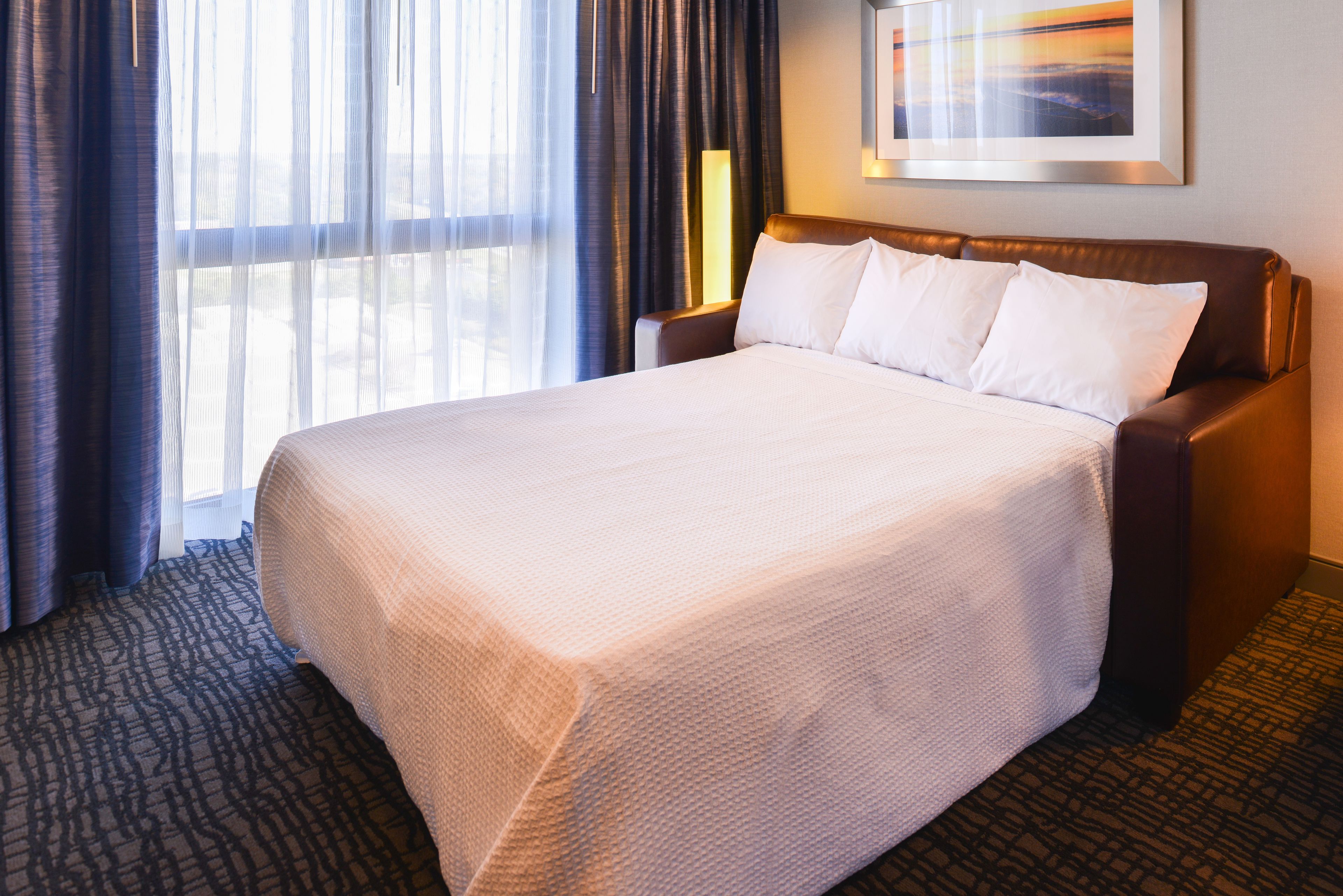A hotel room with a large bed, a nightstand, a lamp, and a window with curtains.