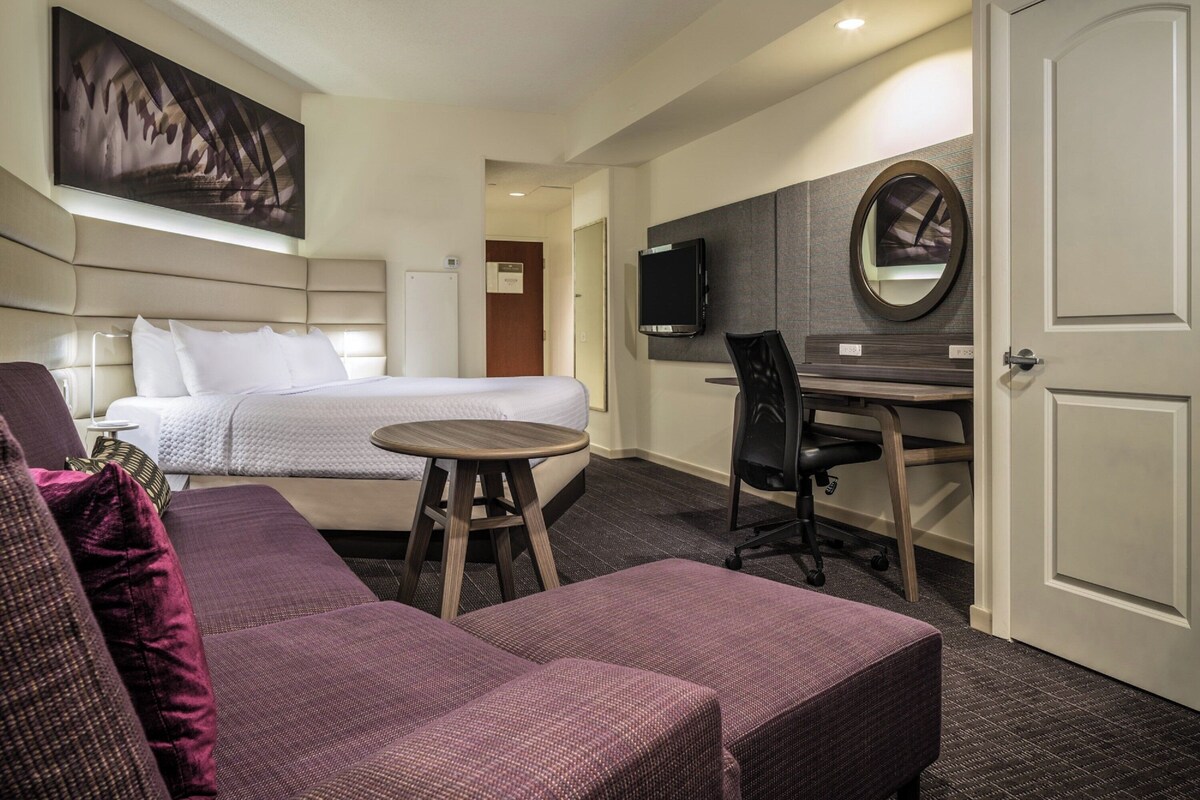 Een hotelkamer met een bed, een bureau, een stoel en een klein rond tafeltje.