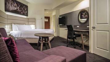 A hotel room with a bed, a desk, a chair, a round mirror, and a television.