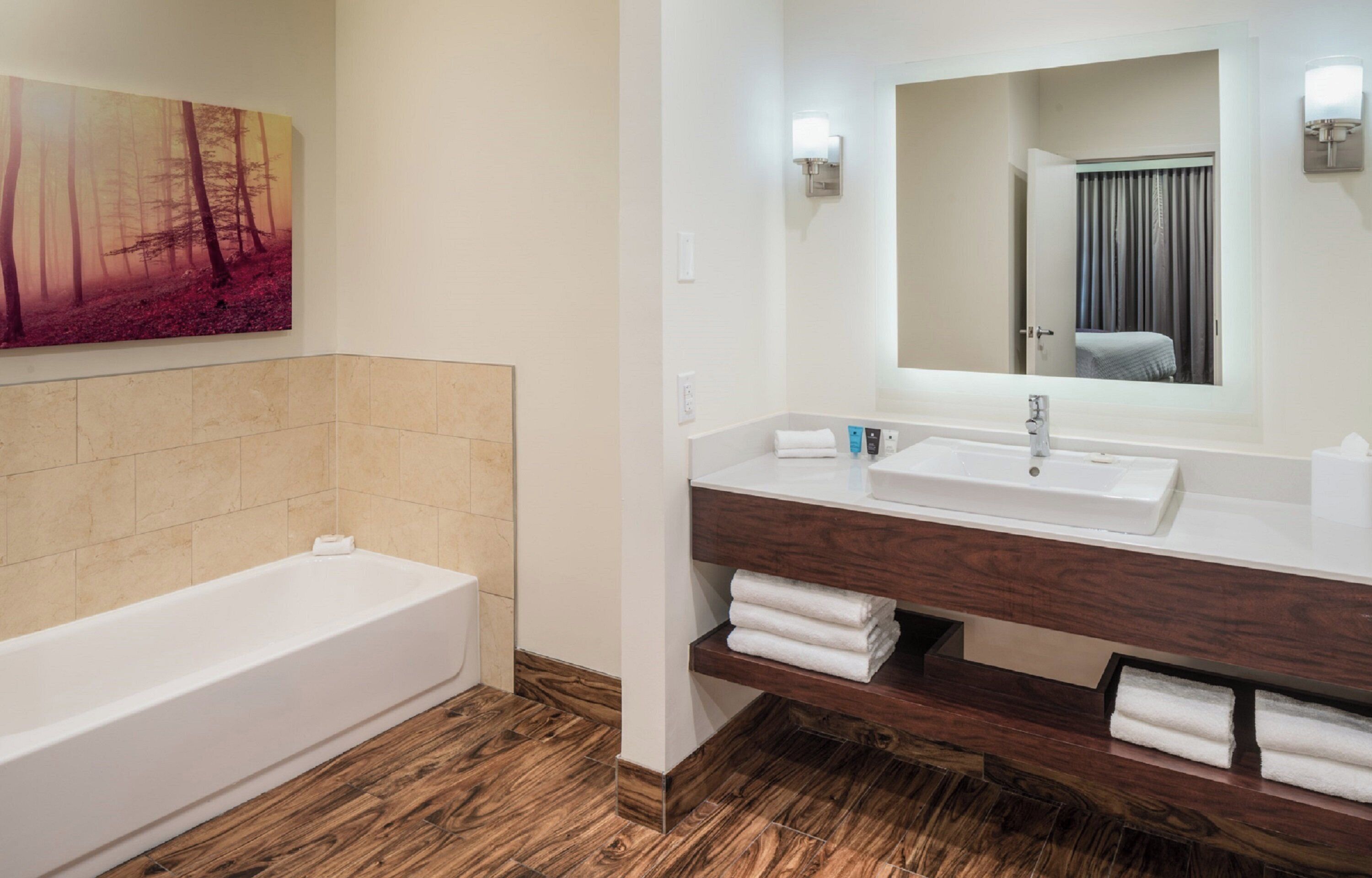 Ein modernes Badezimmer mit Holzboden, einer weißen Badewanne, einem hölzernen Waschtisch mit Spüle und einem großen Spiegel.