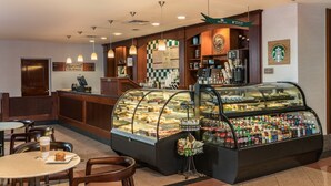 A coffee shop with a bakery display case, seating area, and Starbucks logo.